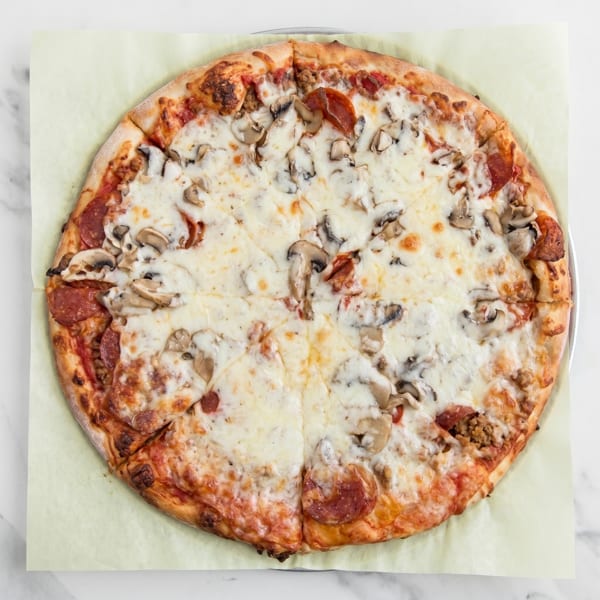A whole pepperoni, sausage, and mushroom pizza on a metal pan with parchment paper.