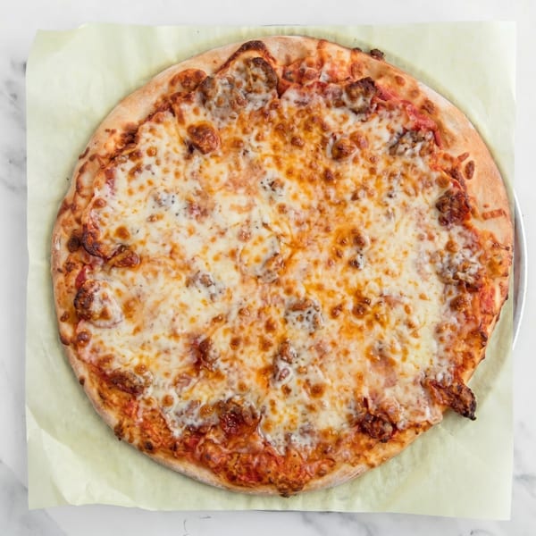 A whole, round pizza with melted cheese and sausage on a light green paper liner.