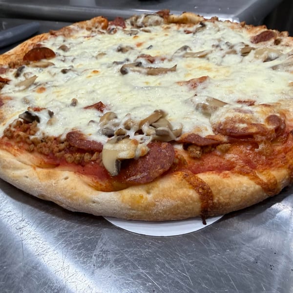 A freshly baked pizza with pepperoni, sausage, mushrooms, and melted cheese on a metal counter.